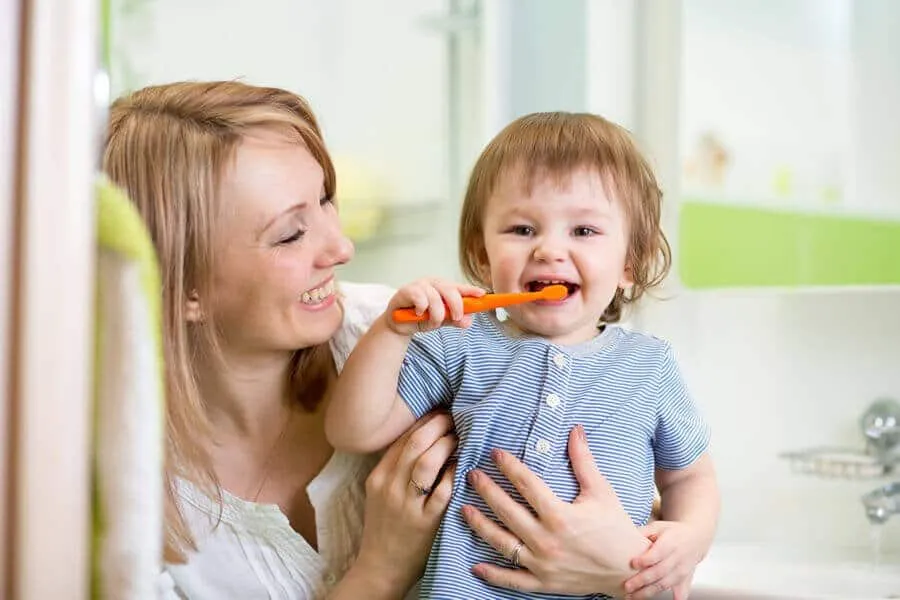 Mother helping her toddler brush his teeth