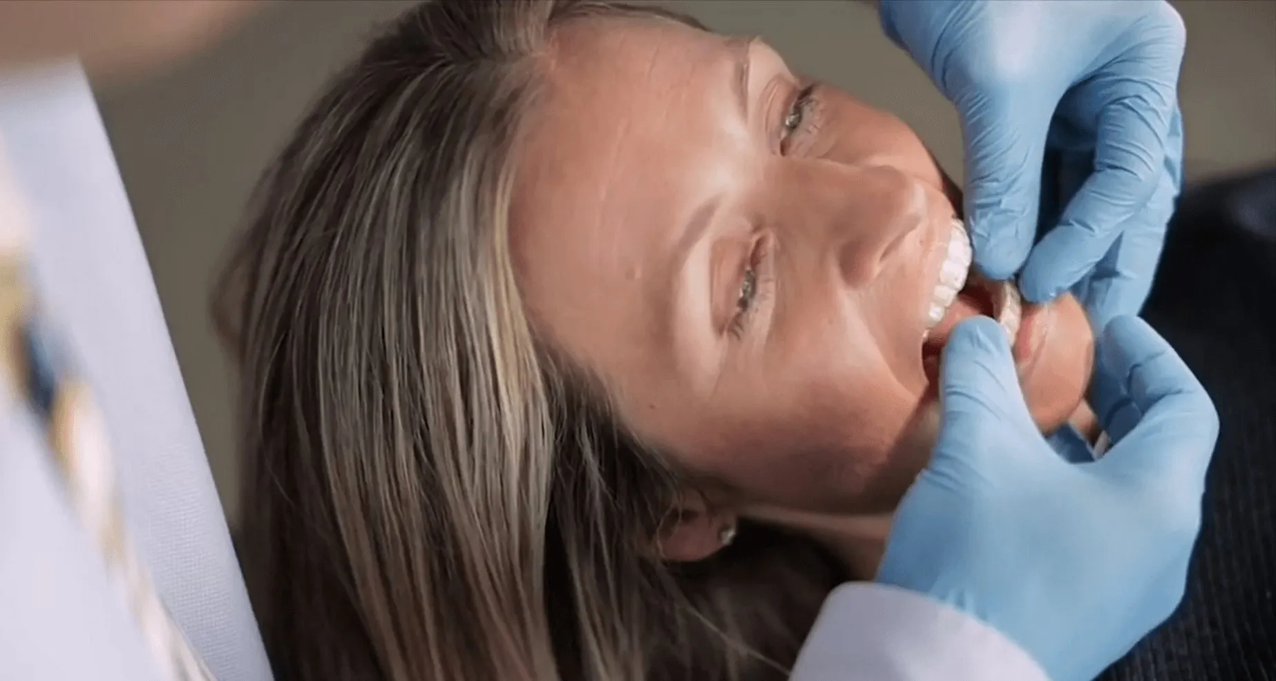 Gloved clinician examining a young patient reclined in the dental chair