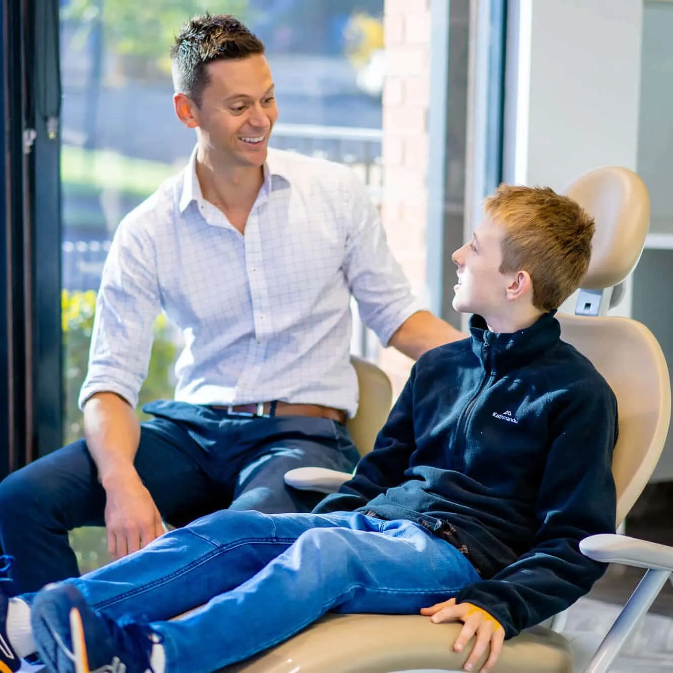 Orthodontist talking with a teenage boy seated in the treatment chair