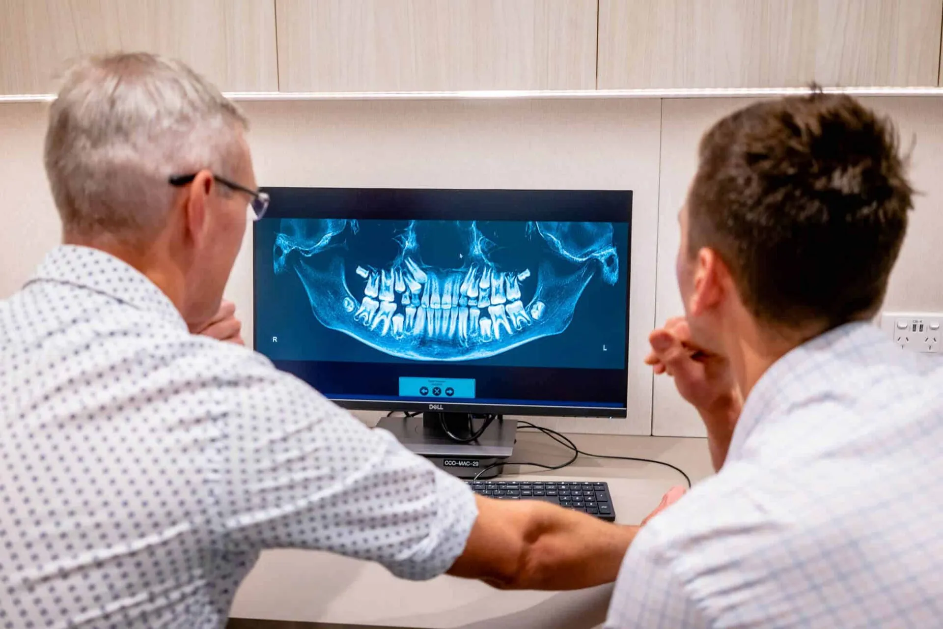 Two orthodontists at a desk reviewing a patient's panoramic jaw x-ray on screen
