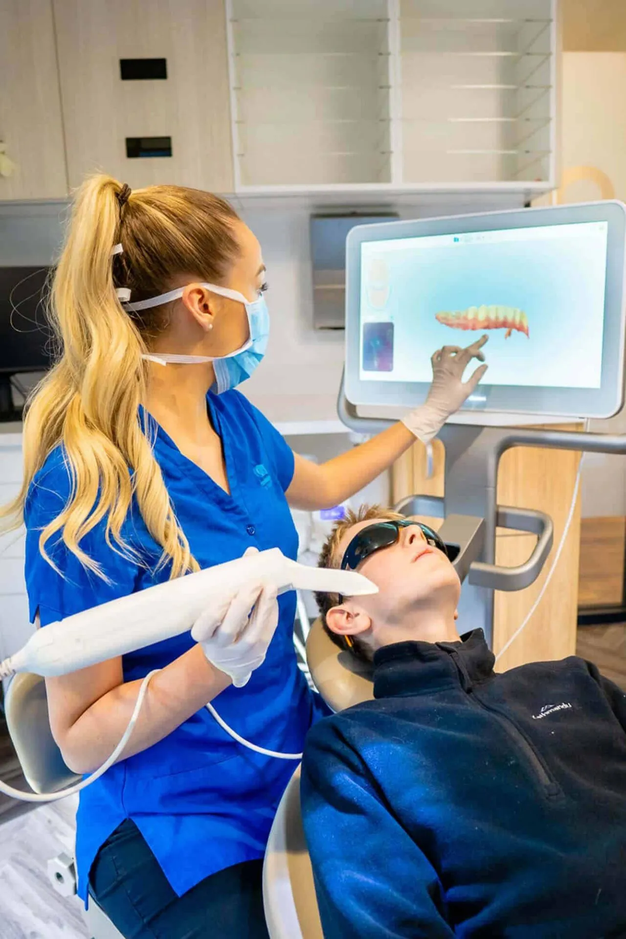 Dental assistant taking a 3D intra-oral scan of a patient, with the scan showing on screen