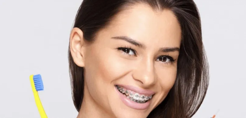Young woman with braces smiling and holding a toothbrush