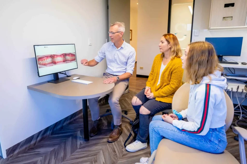 Orthodontist showing treatment images on a screen to a parent and child at a desk