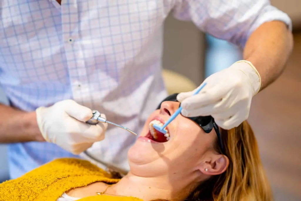 Gloved clinician using a digital scanner in the mouth of a patient wearing safety glasses