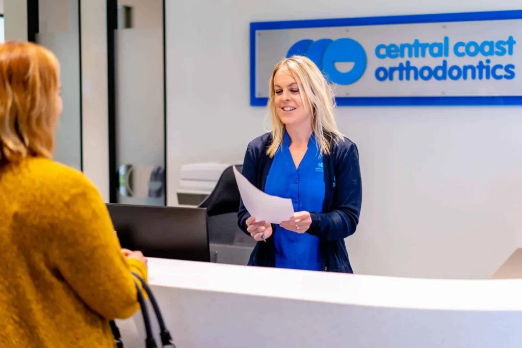 Receptionist handing paperwork to a patient beneath the Central Coast Orthodontics sign