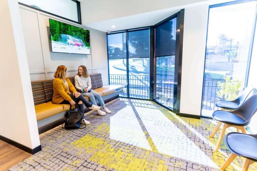 Waiting area with a bench seat, wall-mounted screen and full-height windows