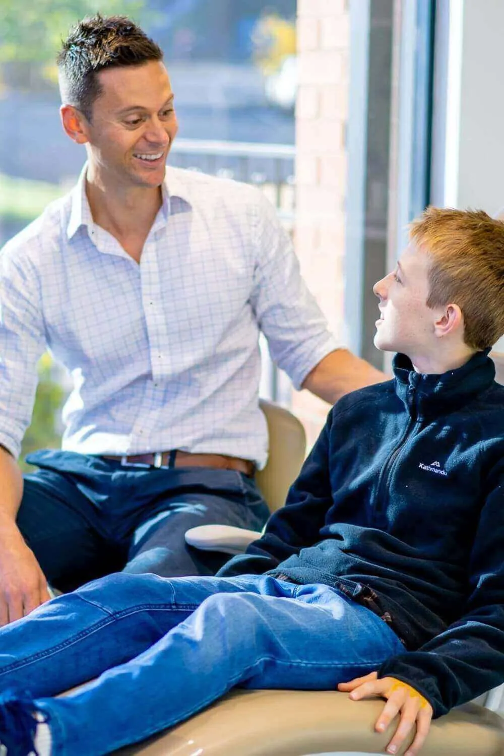 Orthodontist talking with a teenage boy beside the treatment chair