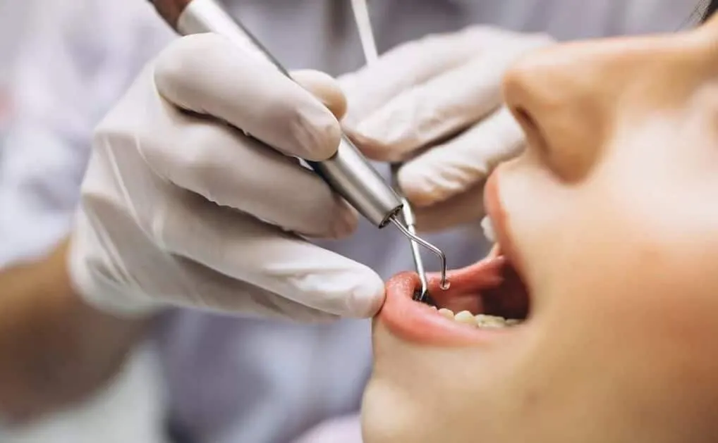 Gloved clinician using an instrument to work on a patient's teeth
