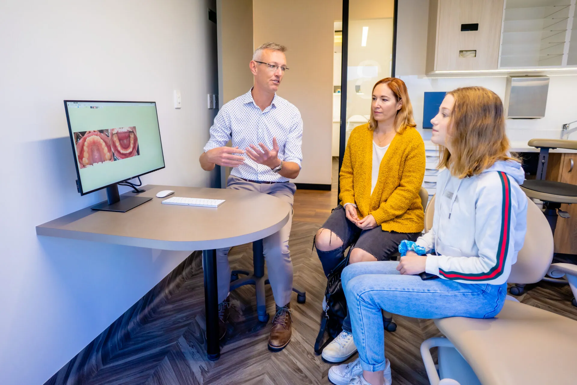 Orthodontist talking with a mother and daughter at a desk in the practice