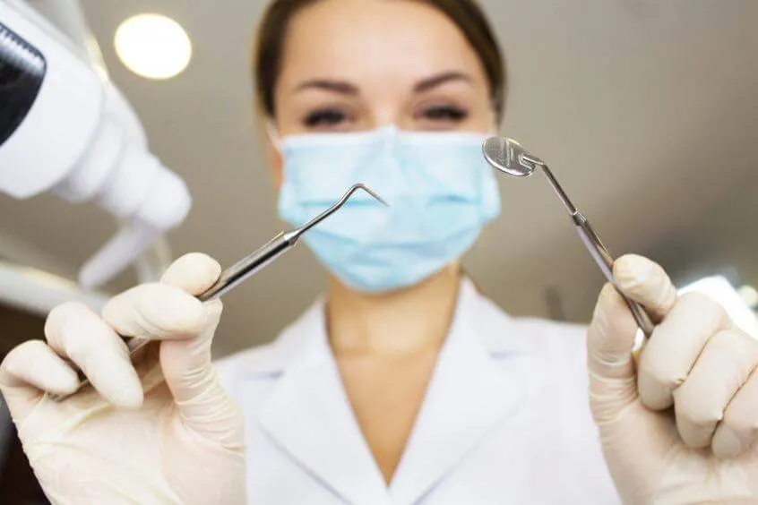Clinician in a mask holding a dental mirror and probe