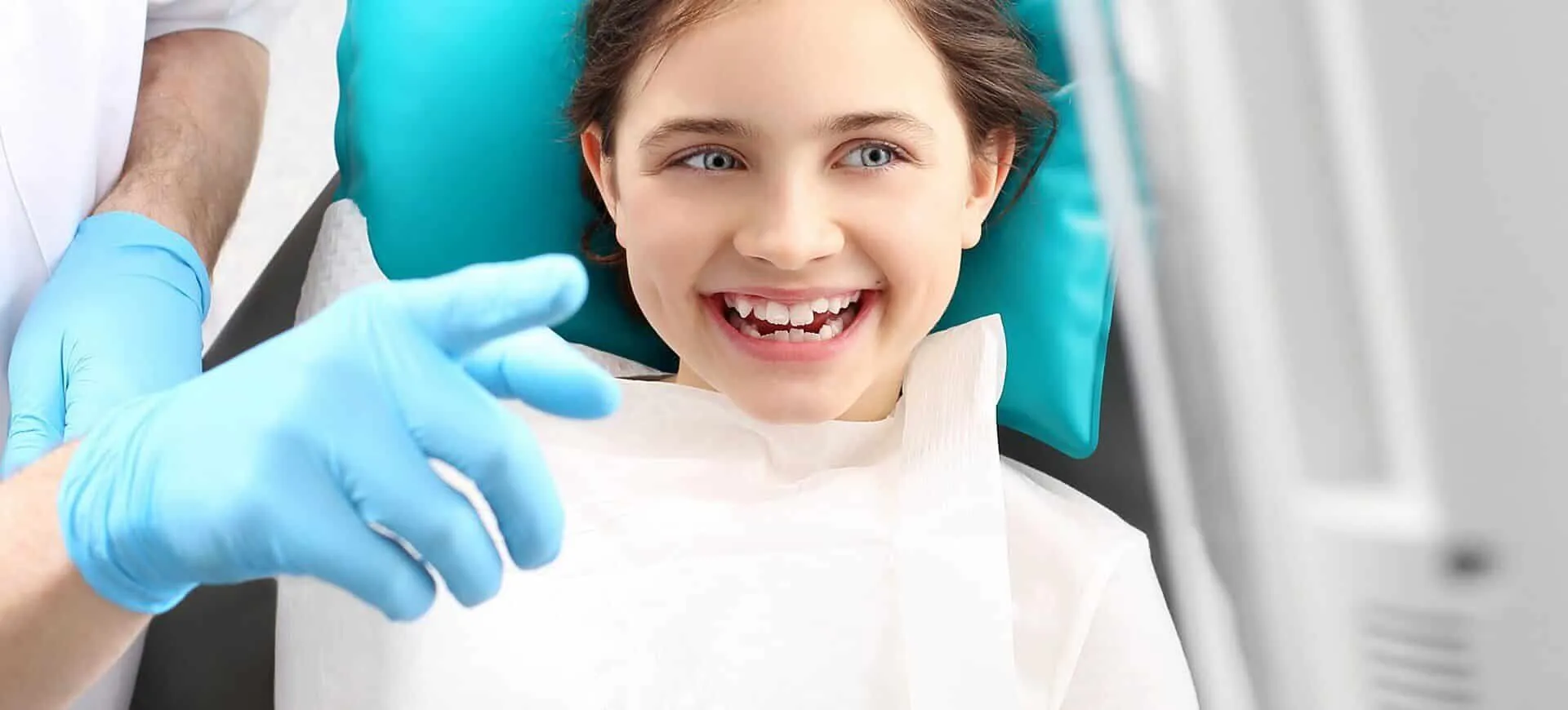 Young girl smiling in the dental chair while a gloved clinician examines her teeth