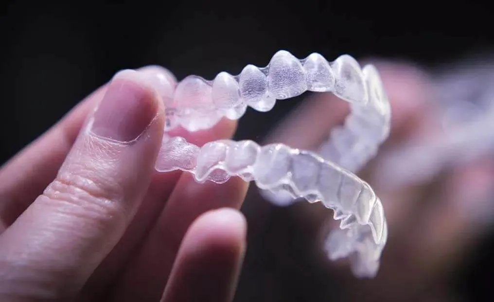 Hands holding a clear aligner tray up to the light