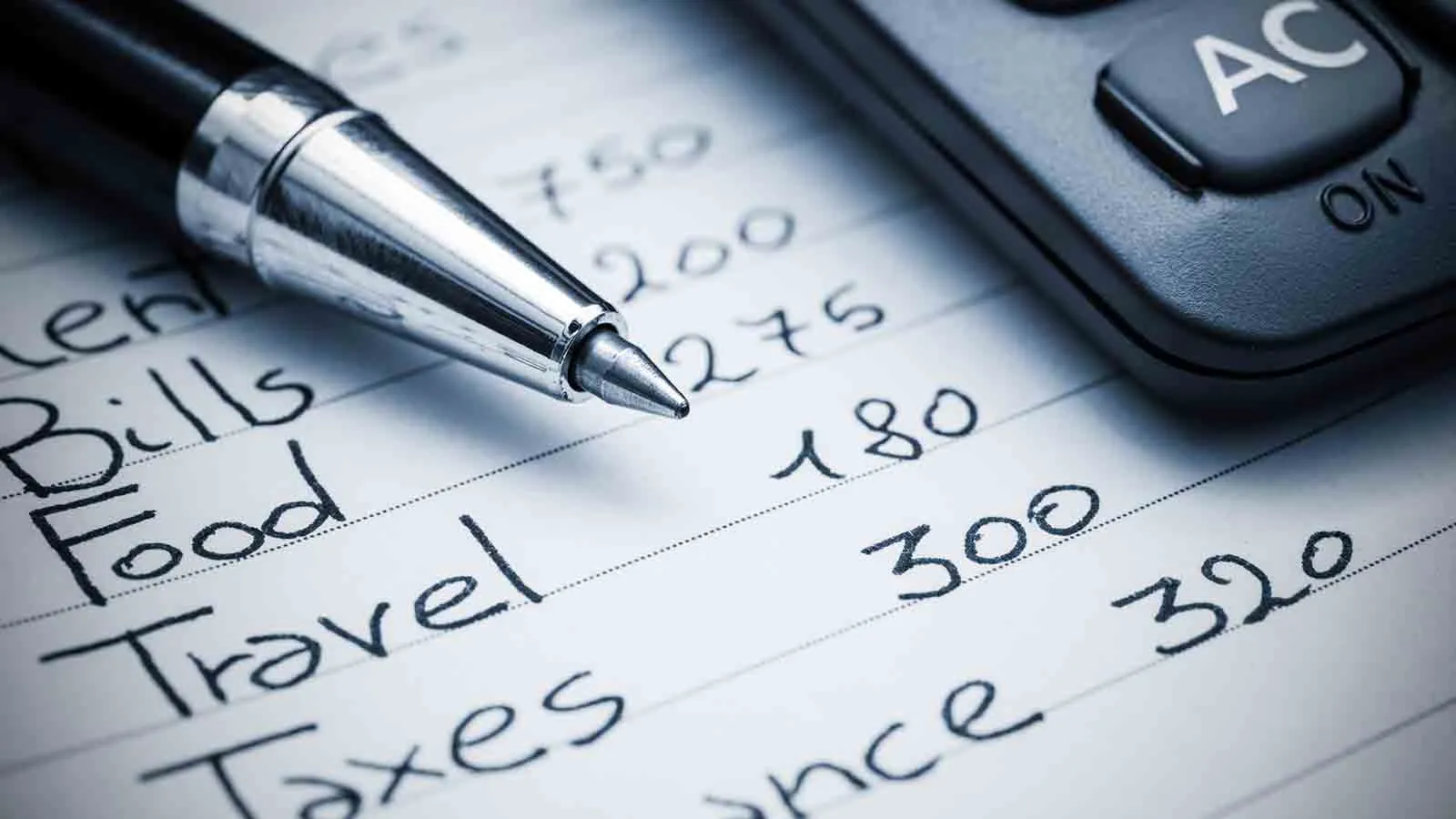 Pen resting on a handwritten household budget listing rent, bills, food, travel and taxes beside a calculator