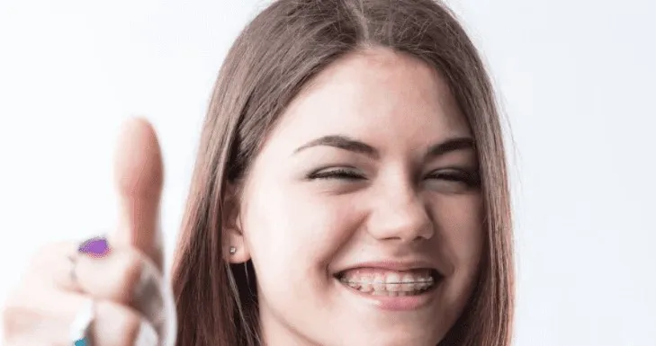 Young woman with braces smiling and giving a thumbs up