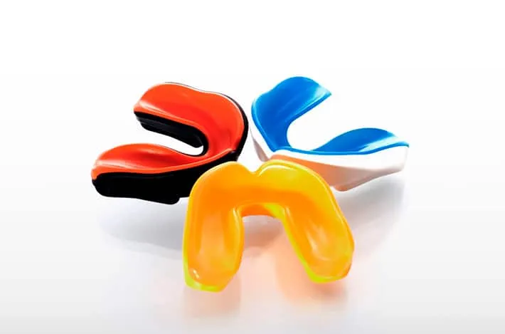 Three coloured sports mouthguards on a white surface