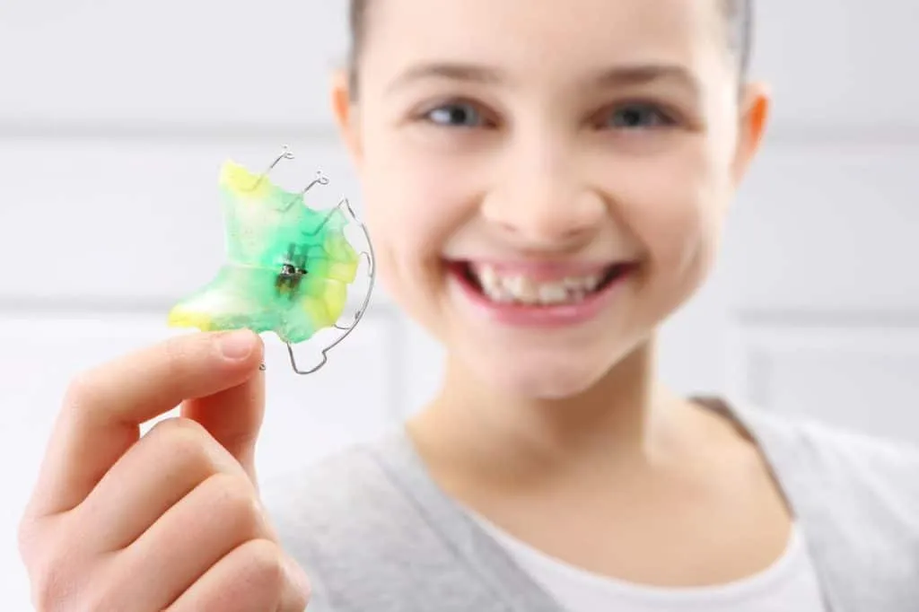 Young girl holding up a colourful removable orthodontic plate