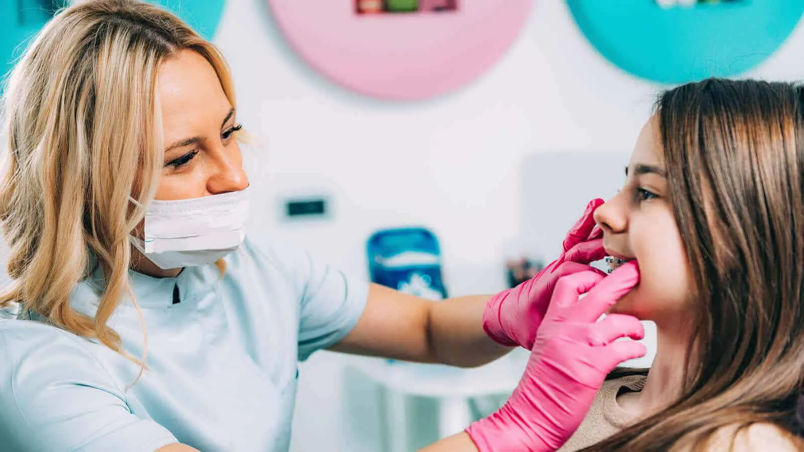 Clinician in a mask fitting an appliance for a smiling young patient