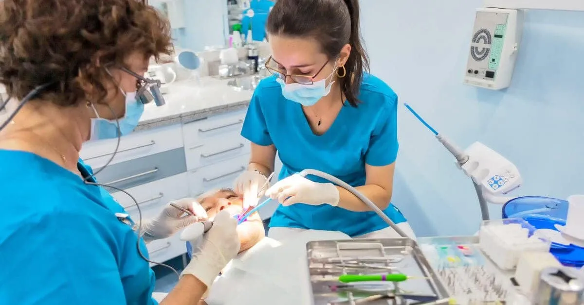 Two clinicians in scrubs treating a patient in the dental chair