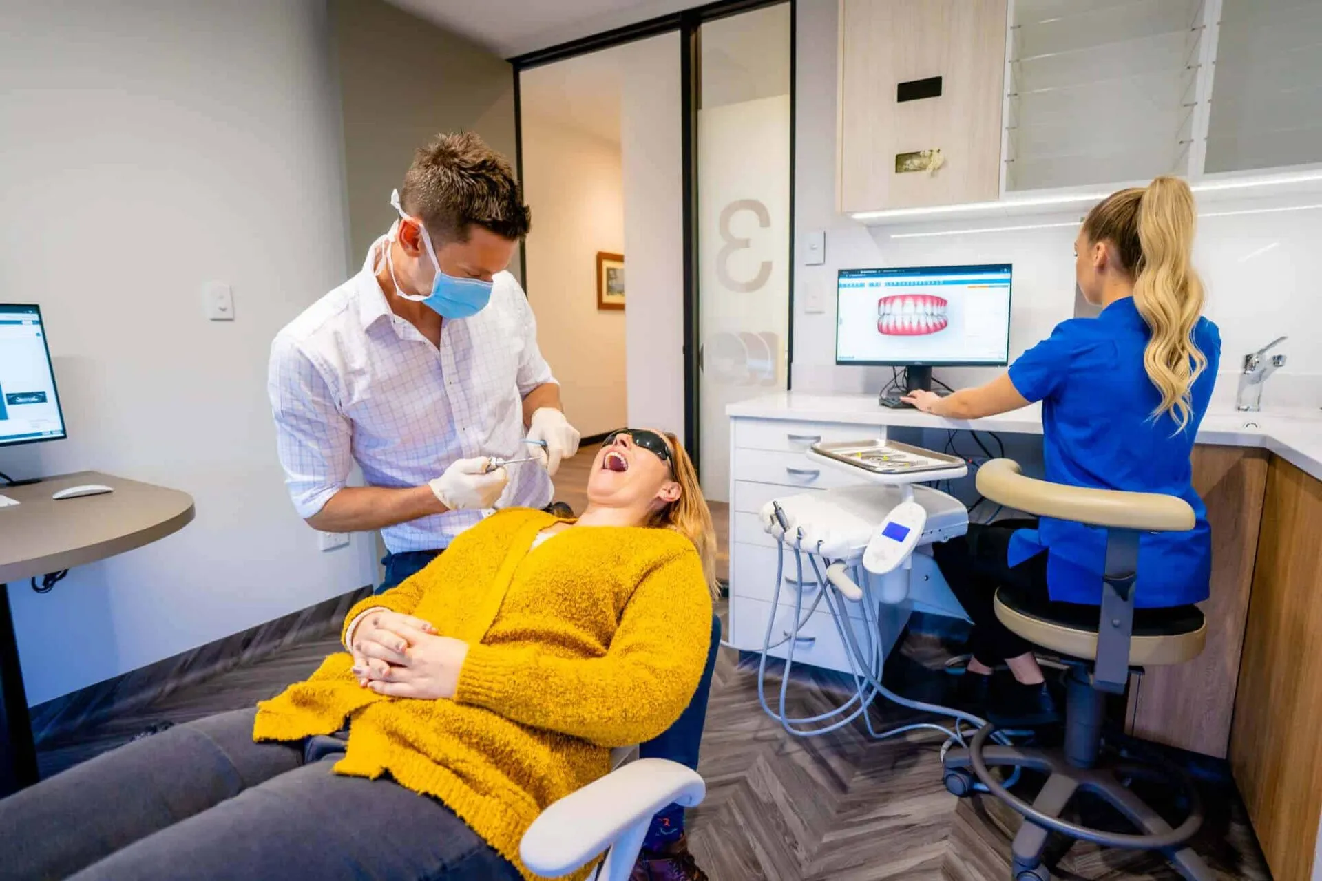 Orthodontist and assistant treating a patient in the chair while a parent watches