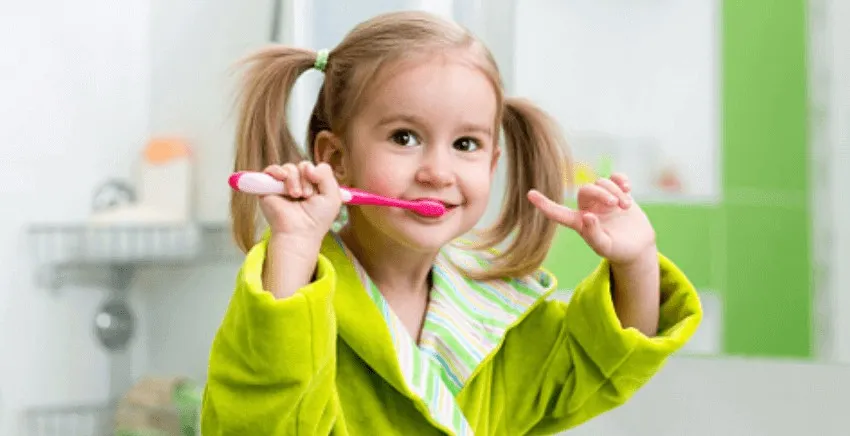 Young girl in a green jacket brushing her teeth