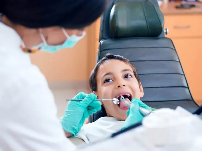 Clinician in a mask examining a young boy's teeth in the dental chair