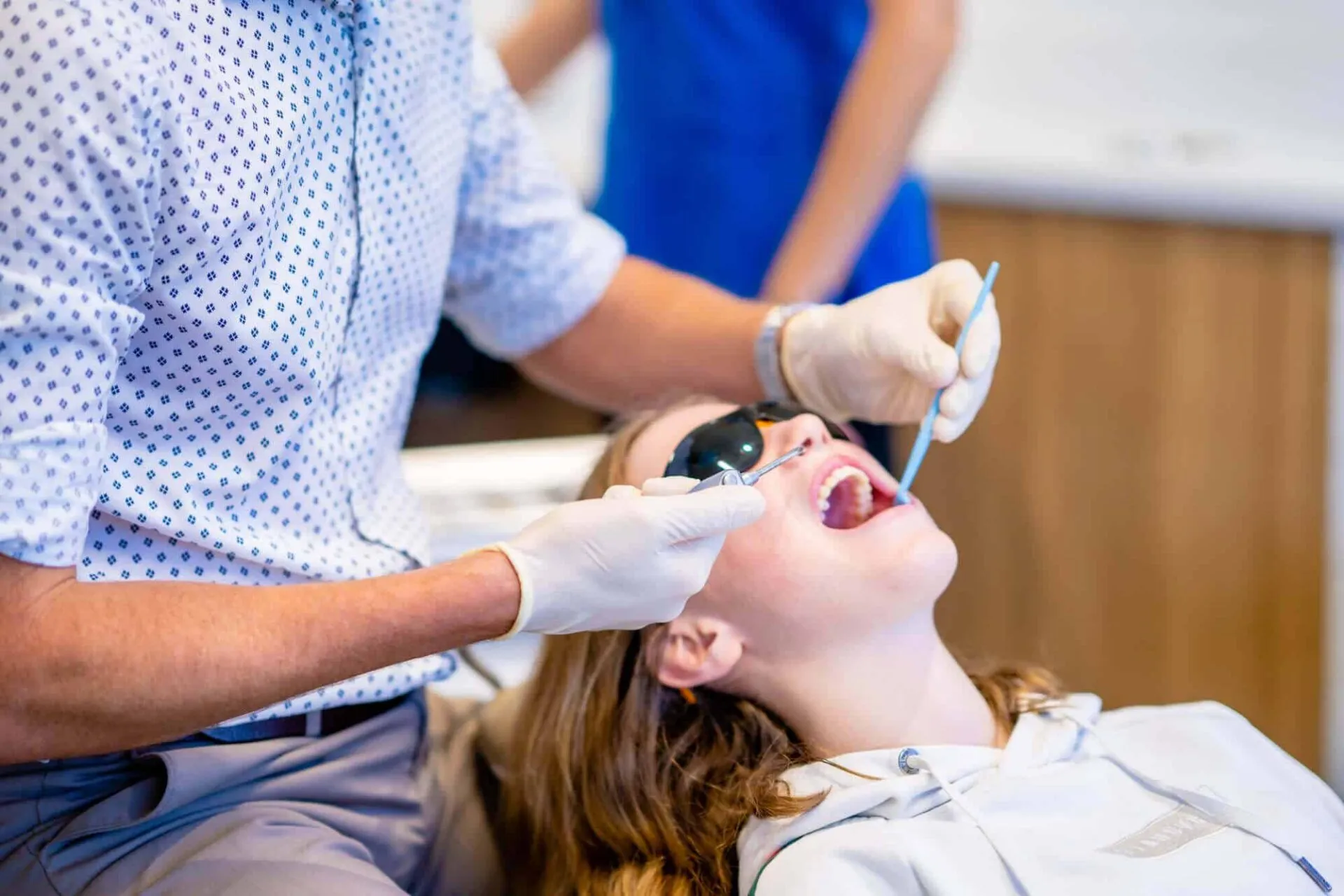 Patient in protective glasses having braces adjusted while an assistant helps