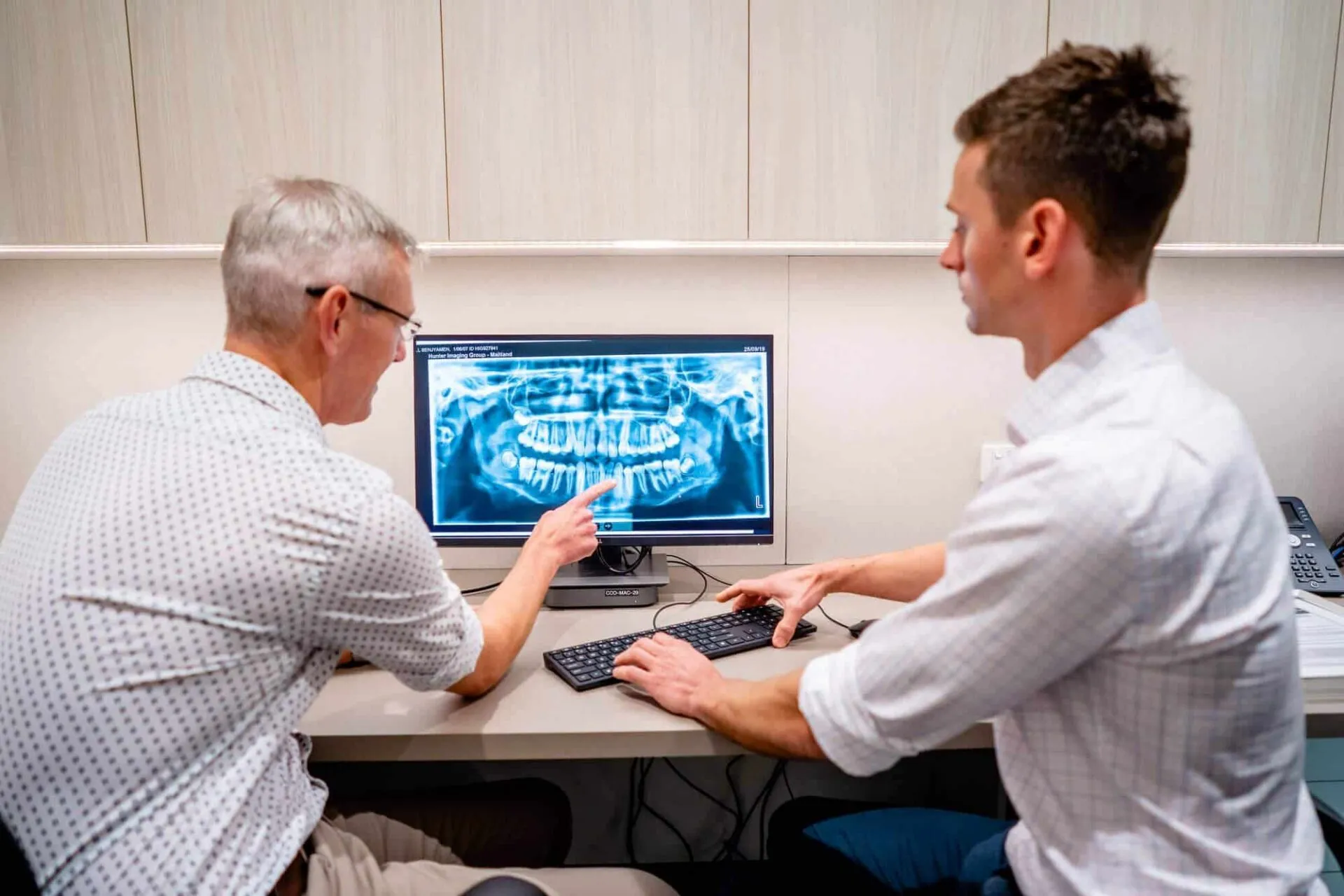 Two orthodontists reviewing a patient's panoramic jaw x-ray on a screen