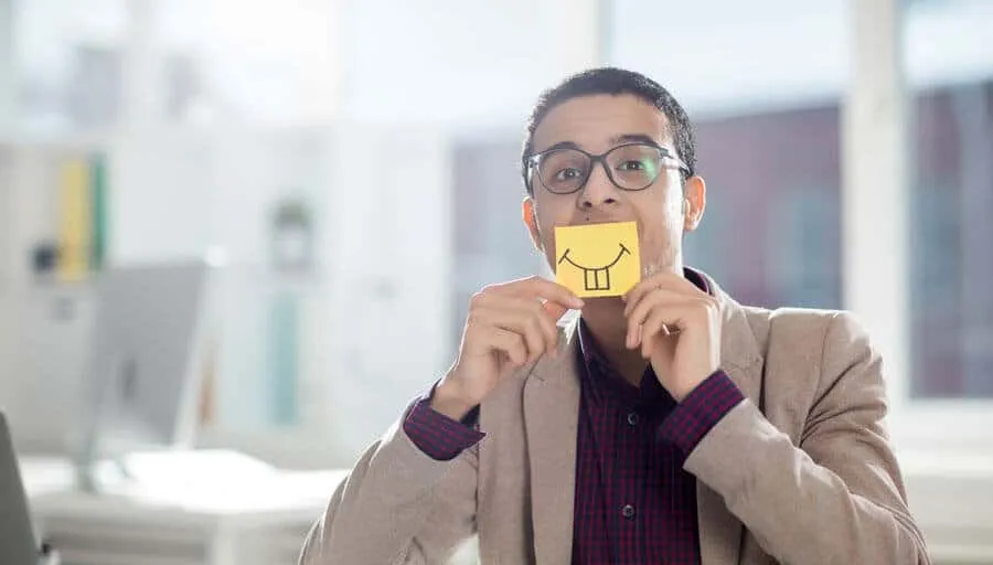 Man in an office holding a small smiley face card in front of his mouth