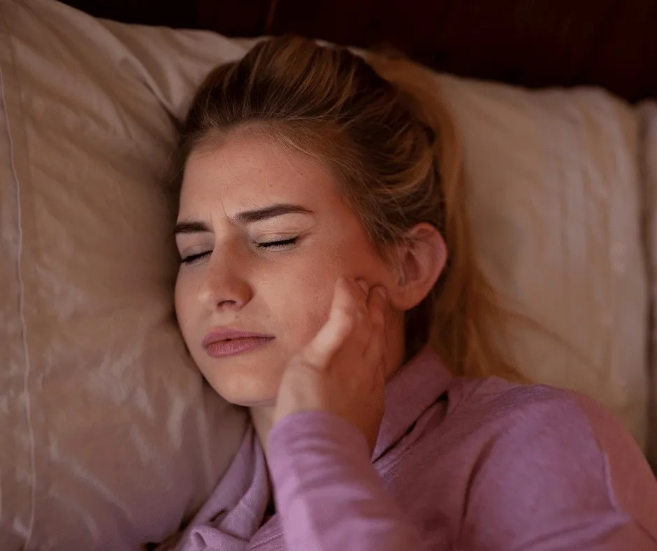 Woman lying in bed holding her jaw in discomfort