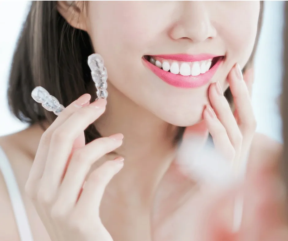 Woman holding a clear aligner tray beside her smile