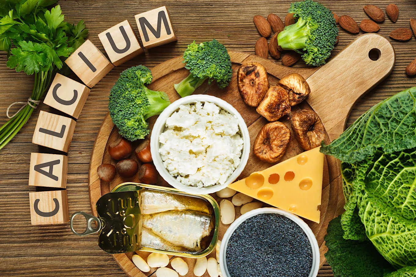 Calcium-rich foods including cheese, yoghurt, almonds, broccoli, kale and sardines arranged around letter tiles spelling CALCIUM