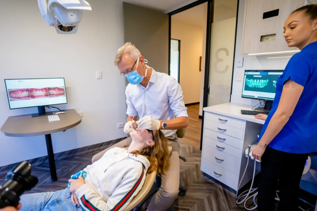 Orthodontist and assistant treating a patient in the chair with images on the screen behind