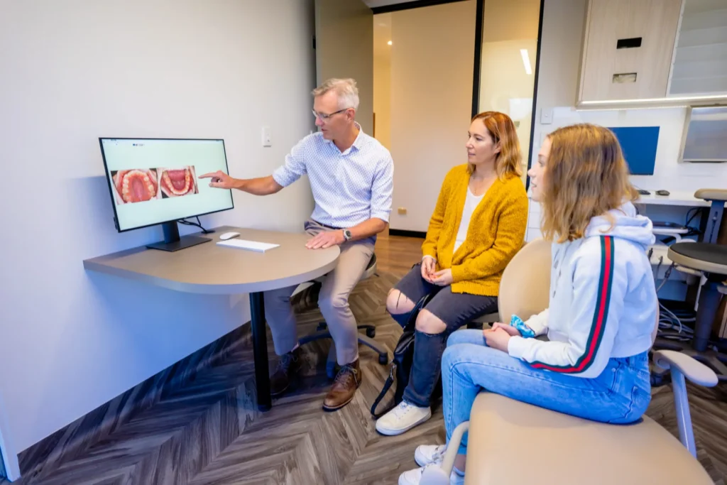 Orthodontist showing treatment images on a screen to a family in the consultation room