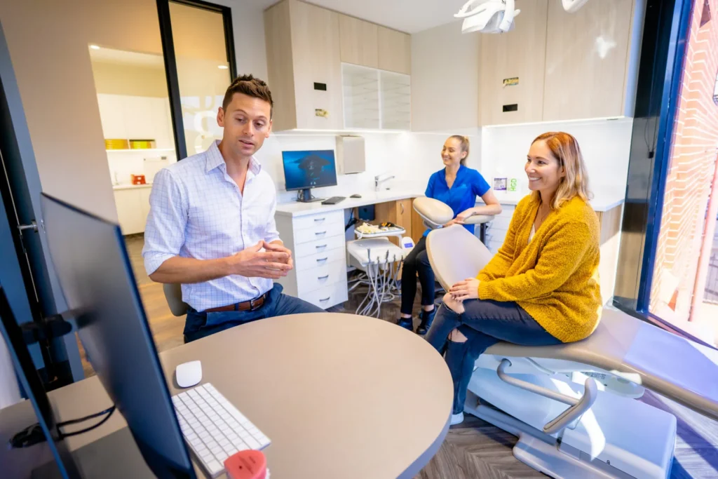 Orthodontist talking with a patient in the treatment room while an assistant works behind