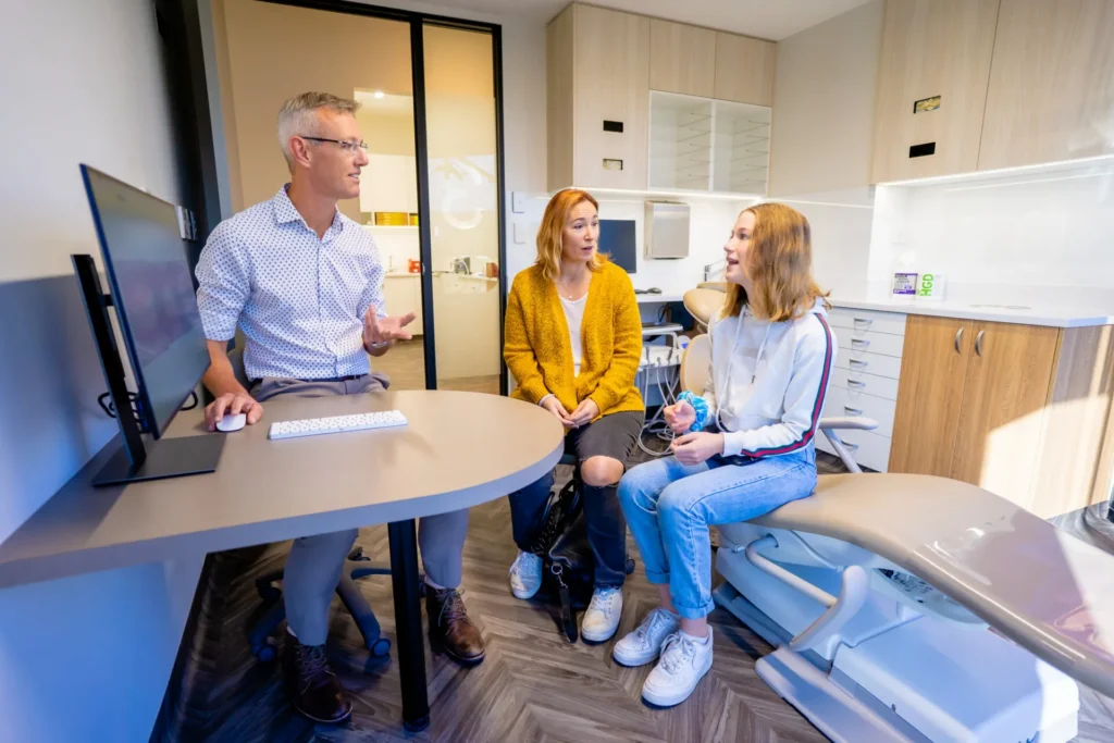 Orthodontist talking with a parent and teenage patient at a desk in the consultation room