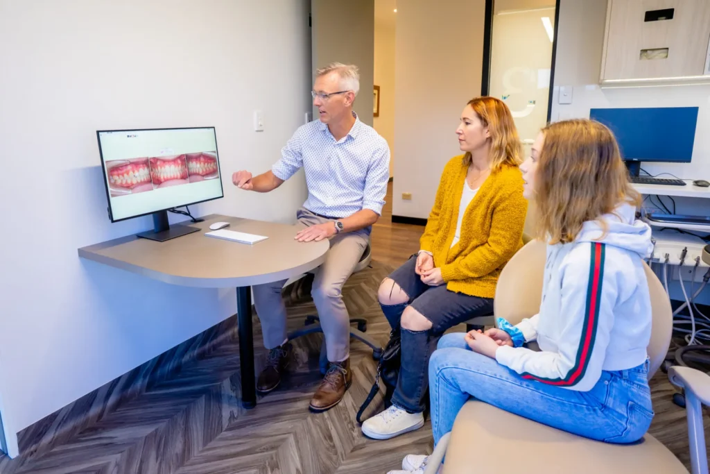 Orthodontist showing treatment images on a screen to a parent and teenage patient