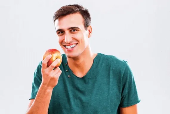 Young man in a green t-shirt smiling and holding an apple