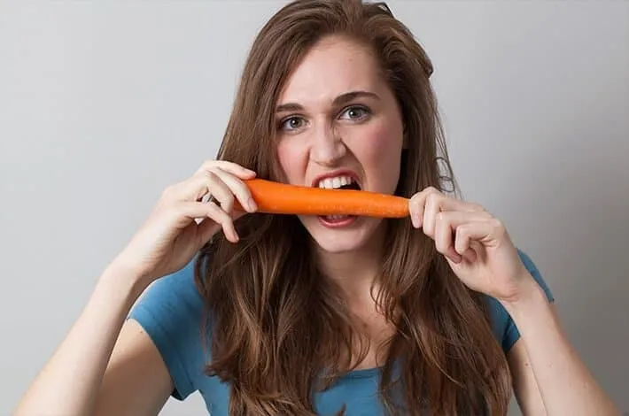 Woman biting into a carrot held in both hands