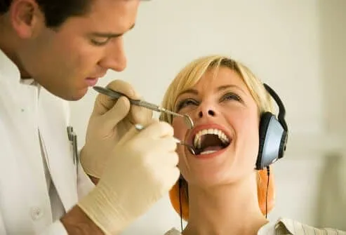 Clinician examining the teeth of a patient wearing headphones in the dental chair
