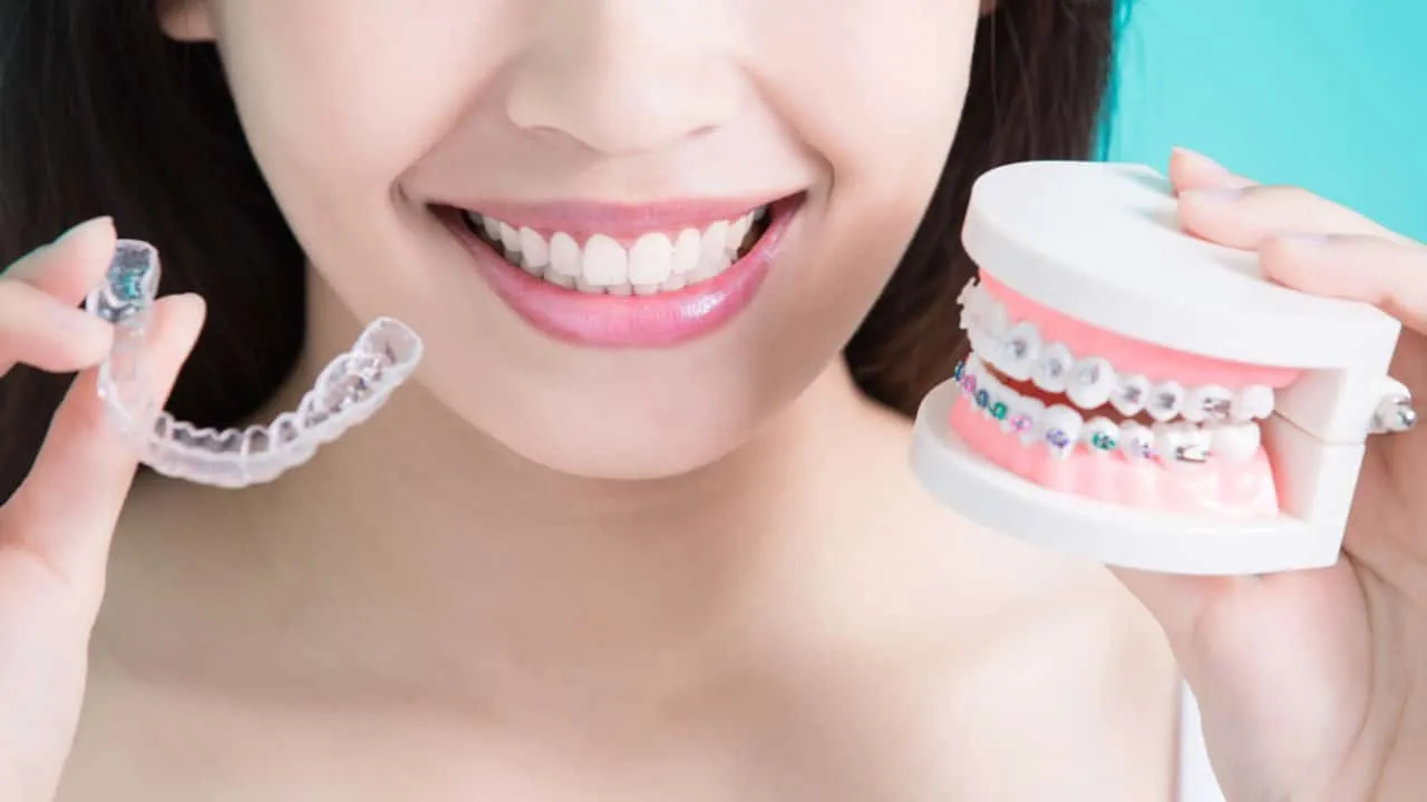 Young woman holding a clear aligner in one hand and a model of braces in the other