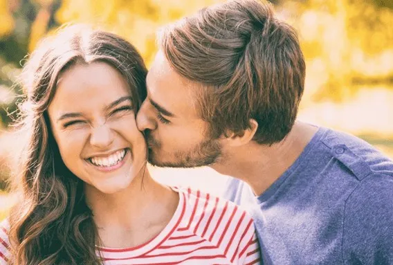 Young man kissing a laughing woman on the cheek, both smiling