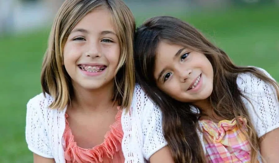 Two young girls smiling outdoors, one of them wearing braces