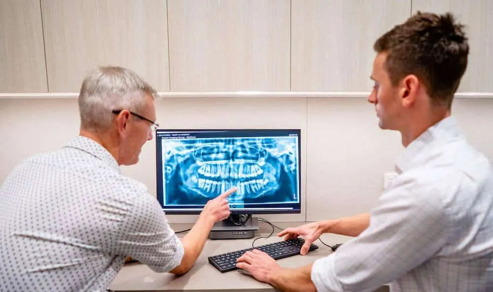 Two orthodontists at a desk reviewing a panoramic jaw x-ray on screen