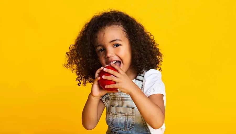 Young girl on a yellow background smiling and holding an apple